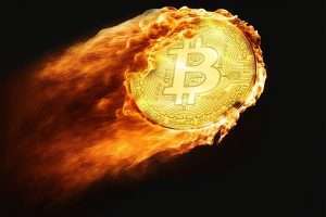 A golden Bitcoin coin engulfed in flames, symbolizing market volatility or a price surge, isolated on a black background.
